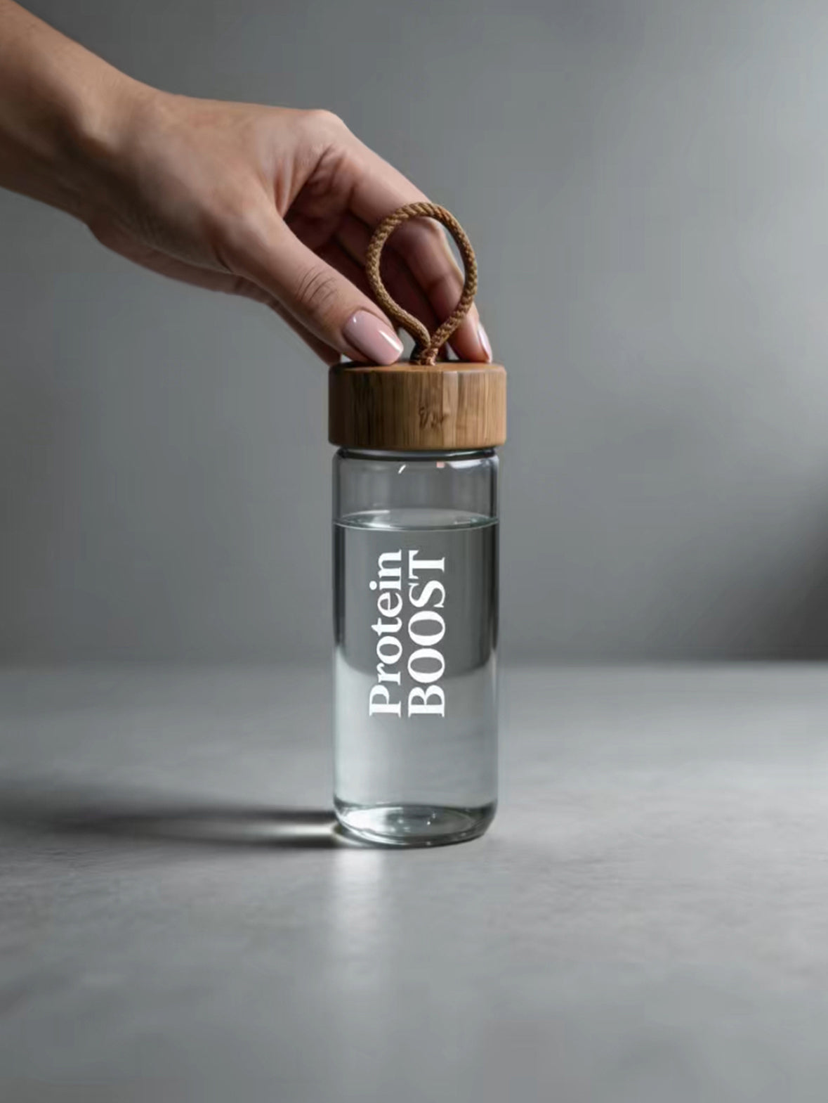 Clear bottle labeled 'Protein BOOST' with a wooden cap held by a hand against a gray background