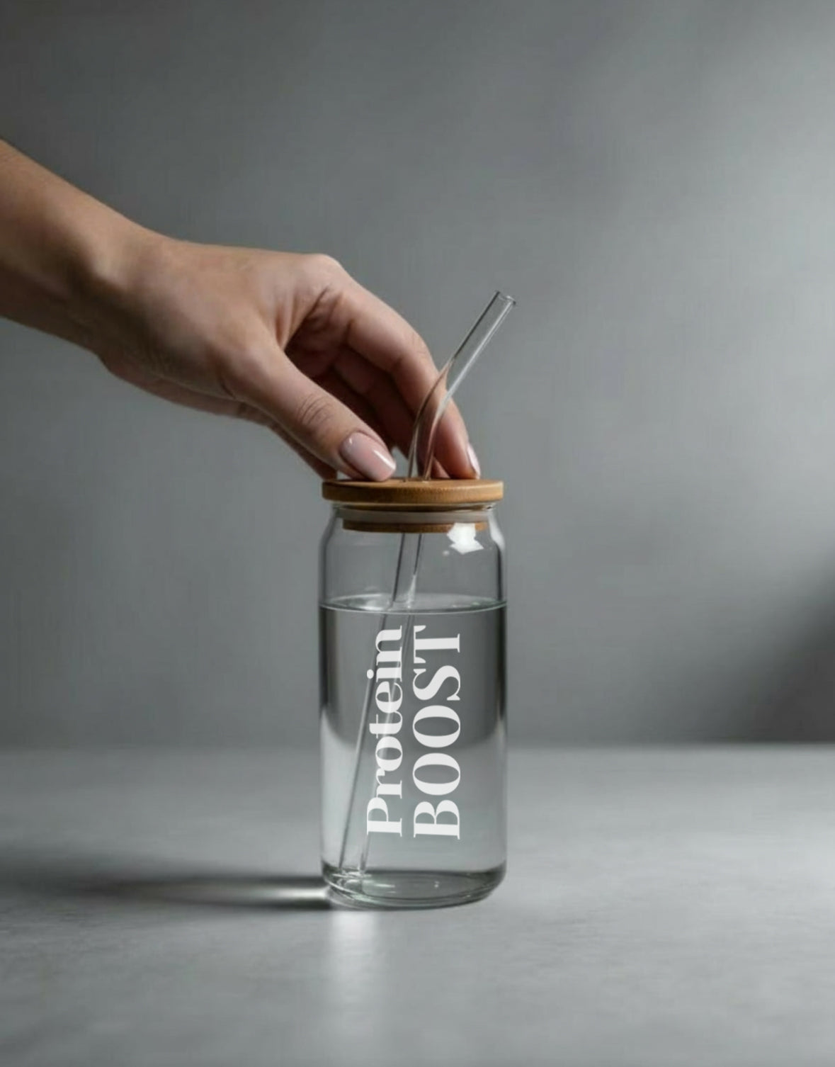 Clear glass bottle labeled 'Protein Boost' with a wooden cap and straw on a gray background